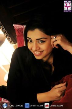 a woman sitting on top of a bed holding a cell phone to her ear and smiling at the camera