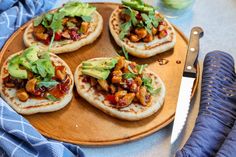 four pita breads on a wooden platter with avocado and other toppings