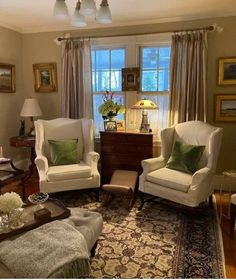 a living room with two chairs and a rug in front of a window that has curtains on the windowsill