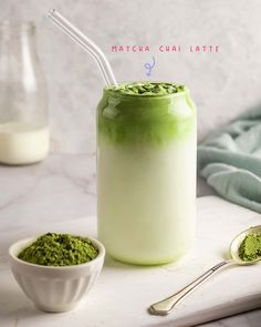 a jar filled with green powder next to two spoons and a glass full of milk