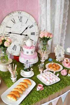 a table topped with cakes and pastries next to a clock