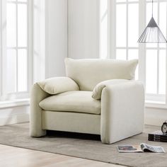 a white chair with pillows on it in front of two windows