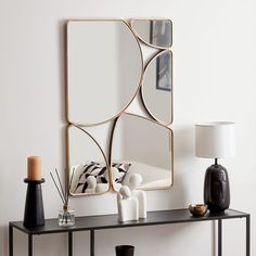 a table with a mirror, vases and other items on it in front of a white wall