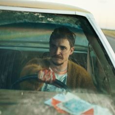 a man sitting in the passenger seat of a car with his hand on the steering wheel