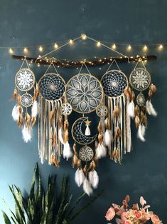 a wall hanging with several dream catchers and lights on top of it, next to a potted plant