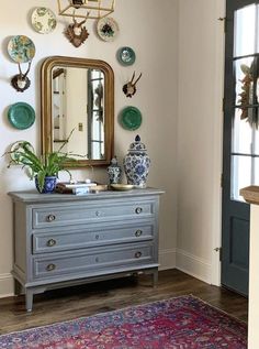 a room with a dresser, mirror and vases on the wall next to it