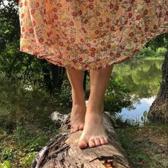 a woman standing on top of a tree log next to a body of water with trees in the background