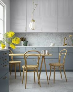 a kitchen with white cabinets and yellow flowers on the countertop, along with two wooden chairs