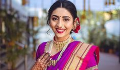 a woman in a purple sari and gold jewelry poses for the camera with her hands on her chest