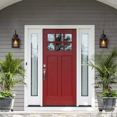 a red front door with two potted plants on either side and one light on