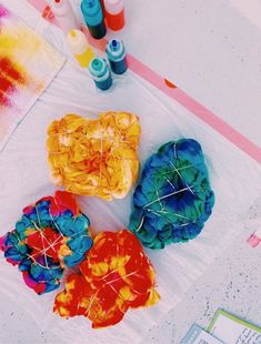 four different colored objects are sitting on the table next to some markers and paintbrushes