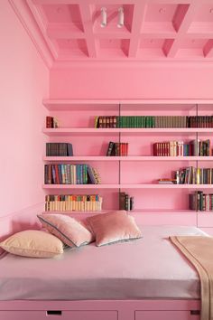 a bedroom with pink walls and bookshelves on the wall, along with a bed