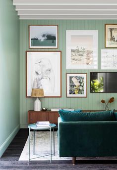 a living room with green walls and pictures on the wall above the couch, along with a coffee table