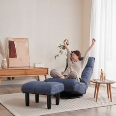 a woman sitting on a blue chair with her arms up in the air and one foot raised