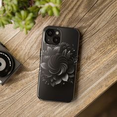 an iphone case sitting on top of a wooden table next to a camera and plant