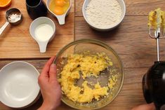 someone mixing ingredients in a bowl on a wooden table next to bowls and spoons