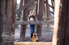 a woman leaning on a wooden fence holding a guitar