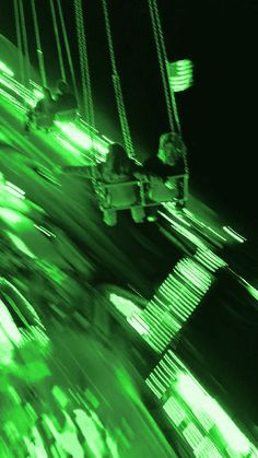 two people on a swing ride at night time with green lights in the dark behind them