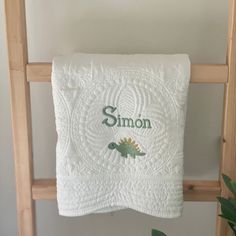 a towel hanging on a wooden ladder with the name simon printed on it and a green dinosaur