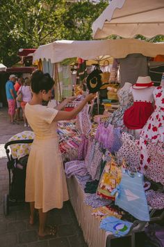 a woman in a yellow dress is looking at some items for sale on a table