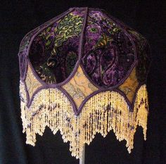 a purple and yellow lamp shade with beads hanging from it's sides on a black background