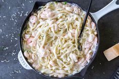 a skillet filled with pasta and shrimp on top of a black counter next to a spatula