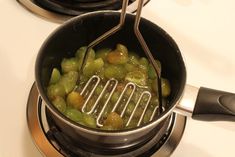 grapes are being cooked in a pot on the stove top, with tongs sticking out