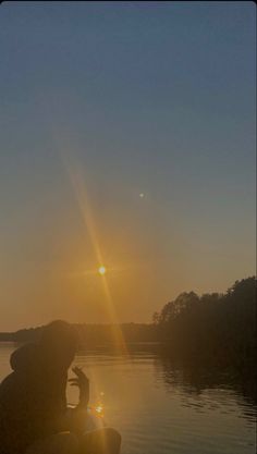 the sun is setting over a body of water with a person sitting on a boat