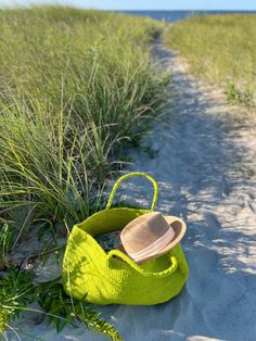 a green bag sitting on top of a sandy beach next to tall grass and sea oats