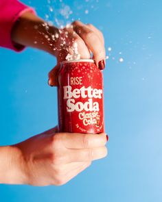 a person is sprinkling water onto a red soda can with the words, rise better soda classic cola