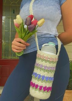 a woman is holding a crocheted bag with flowers in it and water bottle