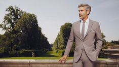 a man in a suit and tie standing on a wall with trees in the background