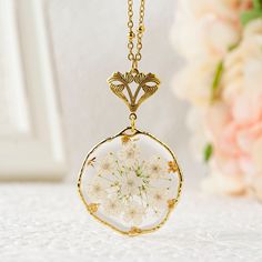 a close up of a necklace on a table with flowers in the background and a vase behind it