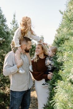 a man and woman with two children in their arms are standing next to each other among the trees