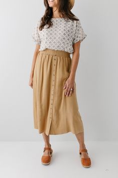 Start your day in style with the 'Greta' Skirt! This midi length, linen-blend skirt is light and airy for spring and summer and features button-down detailing for a fun touch. Pair the 'Greta' with all your favorite tops for Sunday morning or a day at the farmer's market! 30% Linen 70% Rayon Hand Wash Cold Hang to Dry Low Iron if Needed Do Not Dry Clean Fully Lined Model in Ochre Height 5'5" | Wearing Size Small Wearing 'Shalom' Geometric Print Top in Tan & 'Greta' Linen Blend Midi Skirt in Ochr Linen Skirt Outfit Fall, Skirt And Blouse Outfits, Linen Skirt Outfit, Cotton Skirt Outfit, A Line Skirt Outfits, Farmers Market Outfit, Clogs Outfits, Skirt Outfit Fall, Casual Mom Style