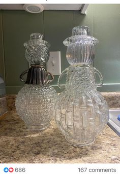 two clear glass vases sitting on top of a counter next to a light switch