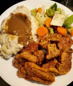 a white plate topped with chicken, mashed potatoes and gravy next to veggies