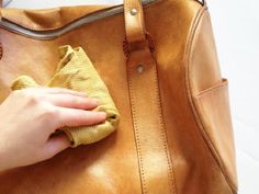 a person is cleaning the inside of a brown leather handbag with a cloth rag