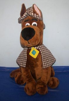 a brown stuffed dog with a hat and scarf on it's head sitting in front of a white wall