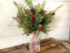 a glass vase filled with red berries and greenery on top of a wooden table