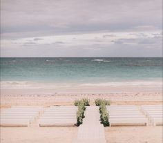 a row of white lawn chairs sitting on top of a sandy beach next to the ocean