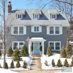 a gray house with white shutters and american flag on the front door in winter