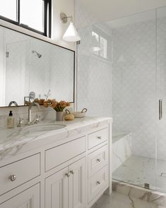 a bathroom with white cabinets and marble counter tops, along with a walk in shower