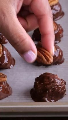 someone picking up some chocolate covered almonds on a baking sheet with their thumb pointing at them