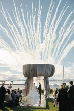 an outdoor wedding ceremony with fireworks in the sky and people sitting on chairs looking at it