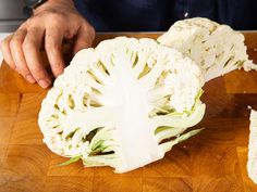 a person cutting up cauliflower on top of a wooden cutting board