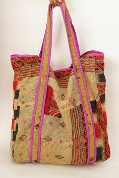 a hand holding a multicolored bag with pink handles and zippers on it