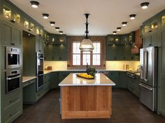 a large kitchen with green cabinets and white counter tops, along with stainless steel appliances