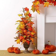 an arrangement of fall leaves and pumpkins in front of a fireplace