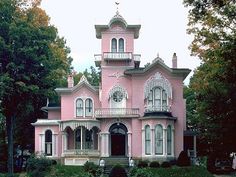 a large pink house with white trim and windows on the top floor is surrounded by greenery